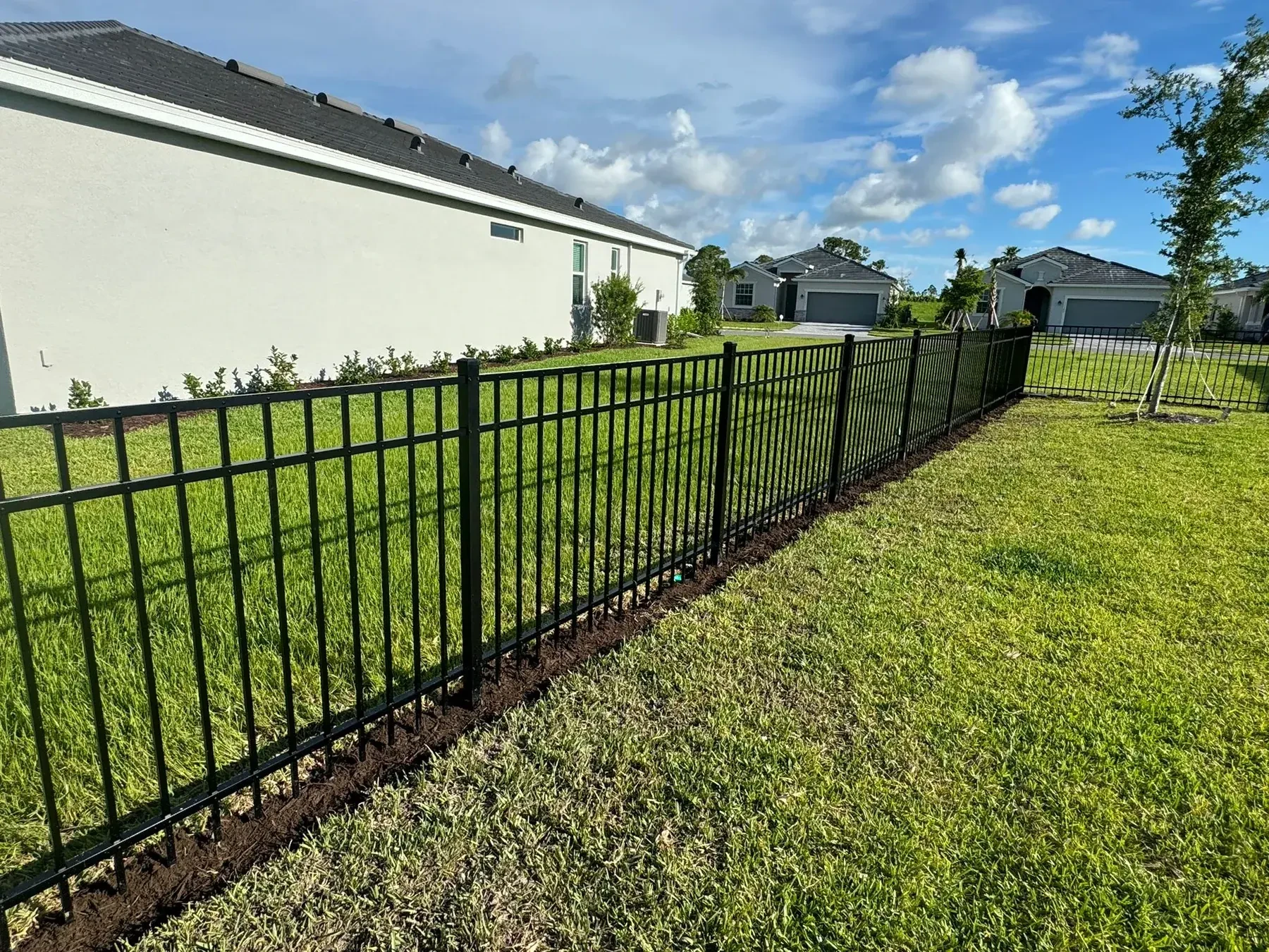 Black aluminum fence with manicured lawn and modern home